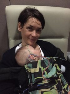 Mother and baby sitting on a chair and the baby has a hearing aid in.