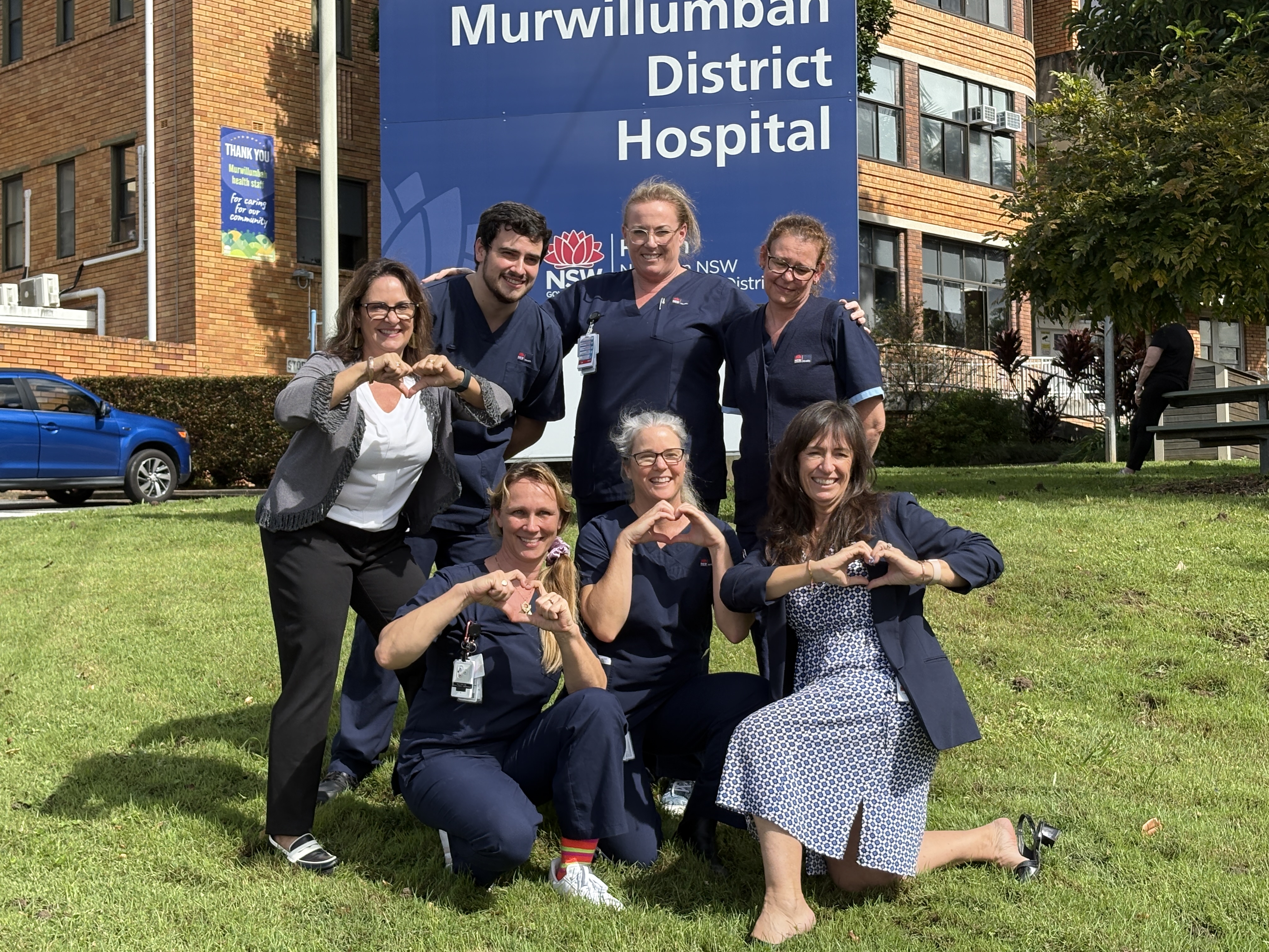 Group of clinical staff holding the love heart symbol outside a hospital