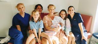 The Espie family, mum holding new baby, with midwifery staff sitting on a couch